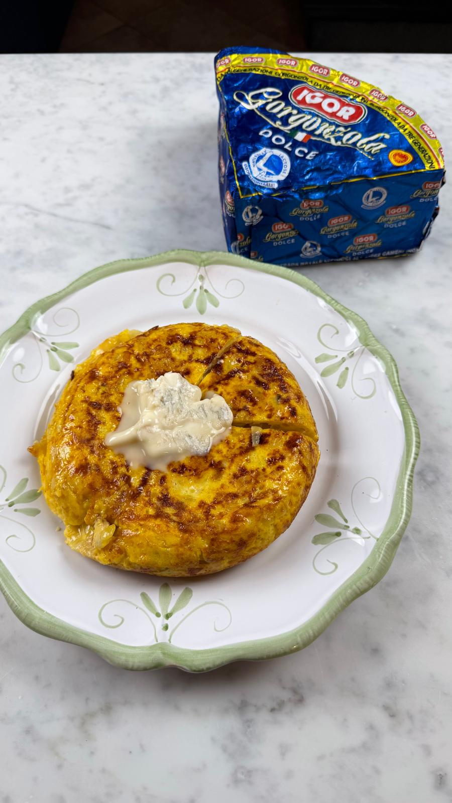 Tortilla di patate con cuore cremoso di Gorgonzola Dolce IGOR, accompagnata da un pacchetto di Gorgonzola IGOR, simbolo di qualità e tradizione italiana.